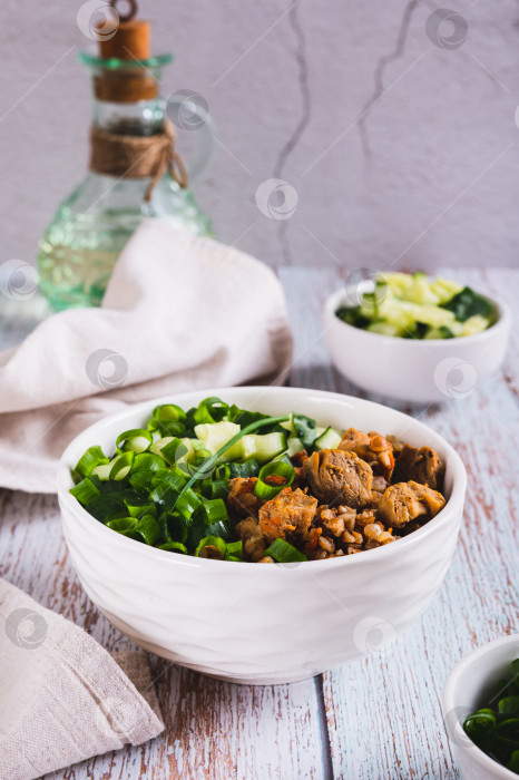 Скачать Гречневая каша с мясом, огурцом и зеленым луком в миске на столе в вертикальном положении фотосток Ozero