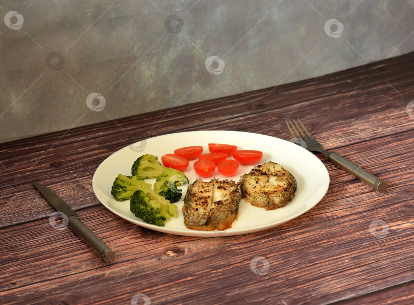 Скачать Два кусочка запеченной белой рыбы, отварная брокколи и свежие помидоры черри на деревянном столе. фотосток Ozero