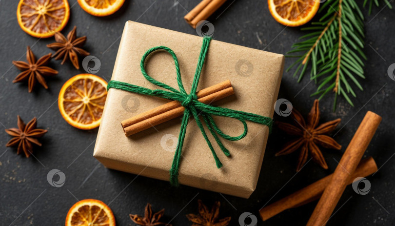 Скачать Новогодний подарок в коробке из крафт-бумаги, перевязанной зеленой лентой. Рождественский фон, ваниль, сушеные апельсины и палочки корицы. Создано с помощью искусственного интеллекта. фотосток Ozero
