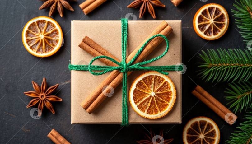 Скачать Новогодний подарок в коробке из крафт-бумаги, перевязанной зеленой лентой. Рождественский фон, ваниль, сушеные апельсины и палочки корицы. Создано с помощью искусственного интеллекта. фотосток Ozero