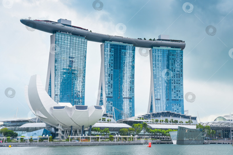 Скачать Сингапур, Сингапур - 4 апреля 2025 года: Знаменитый отель Marina Bay Sands и музей искусства и науки под облачным небом в Сингапуре. Современная архитектура на берегу моря. фотосток Ozero