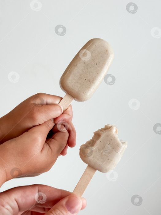 Скачать Две руки держат банановое мороженое на палочках. Крупный план на нейтральном фоне фотосток Ozero