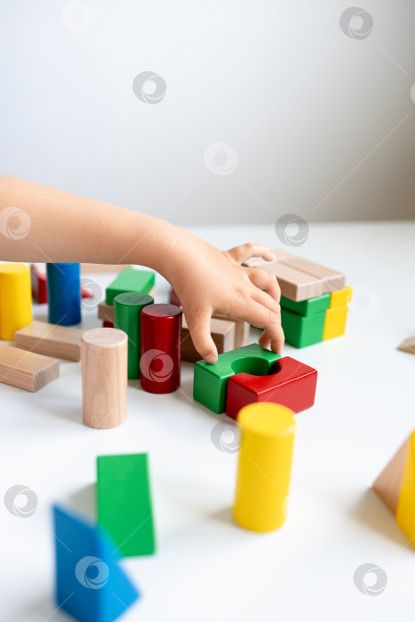 Скачать Ребенок играет с разноцветными деревянными кубиками на белой поверхности фотосток Ozero