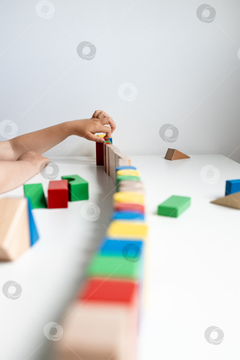 Скачать Ребенок своими руками строит дом из разноцветных деревянных кубиков на белой поверхности фотосток Ozero