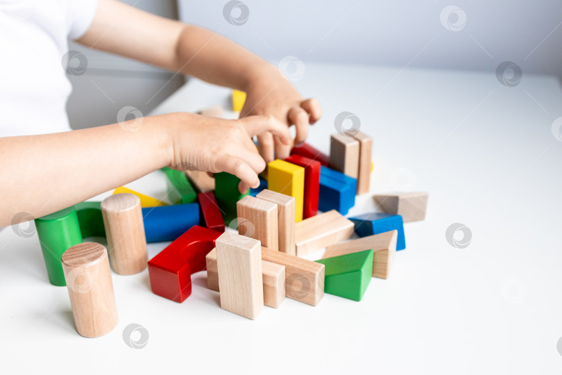 Скачать Ребенок играет с разноцветными геометрическими деревянными кубиками на белой поверхности фотосток Ozero