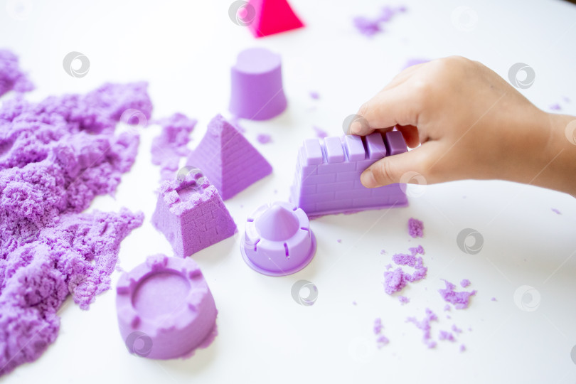 Скачать Детская поделка из фиолетового кинетического песка и формочек на белой поверхности фотосток Ozero