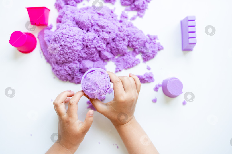 Скачать Детские ручки играют с фиолетовым кинетическим песком и формочками на белом фоне фотосток Ozero