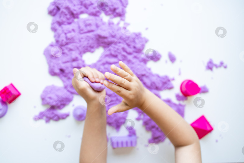 Скачать Детские ручки играют с фиолетовым кинетическим песком и формочками на белом фоне фотосток Ozero