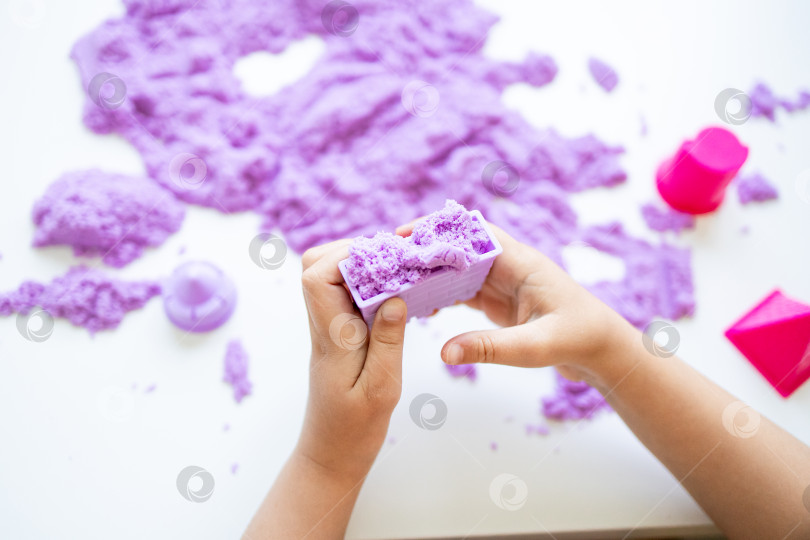 Скачать Ребенок играет с фиолетовым кинетическим песком на белой поверхности фотосток Ozero