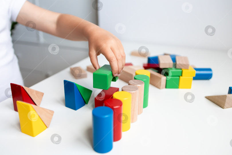 Скачать Ребенок играет с разноцветными геометрическими деревянными кубиками на белой поверхности фотосток Ozero