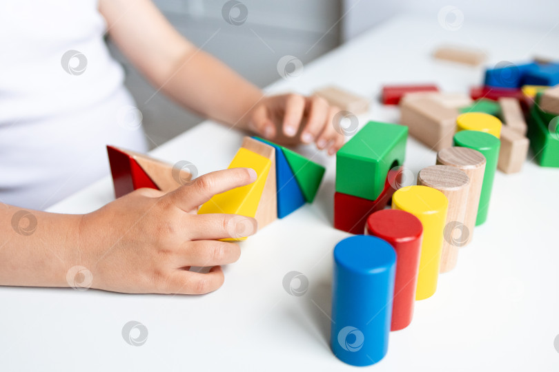 Скачать Ребенок играет с разноцветными геометрическими деревянными кубиками на белом столе фотосток Ozero