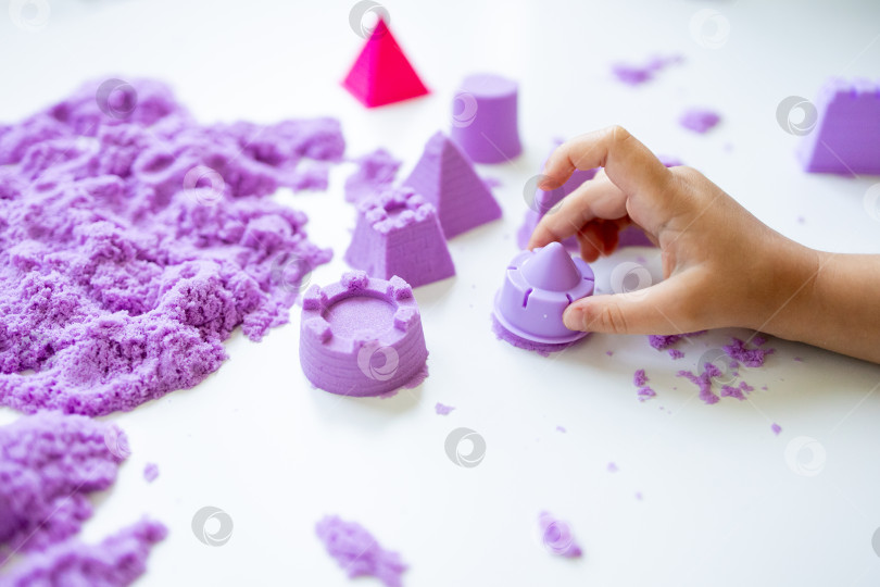 Скачать Детская рука играет с фиолетовым кинетическим песком и формочками фотосток Ozero