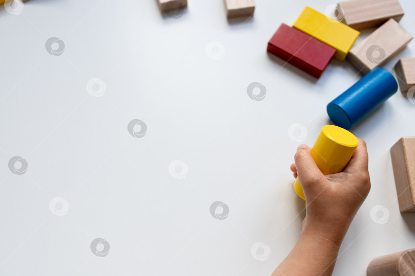 Скачать Детская рука играет с разноцветными деревянными кубиками на белом фоне фотосток Ozero