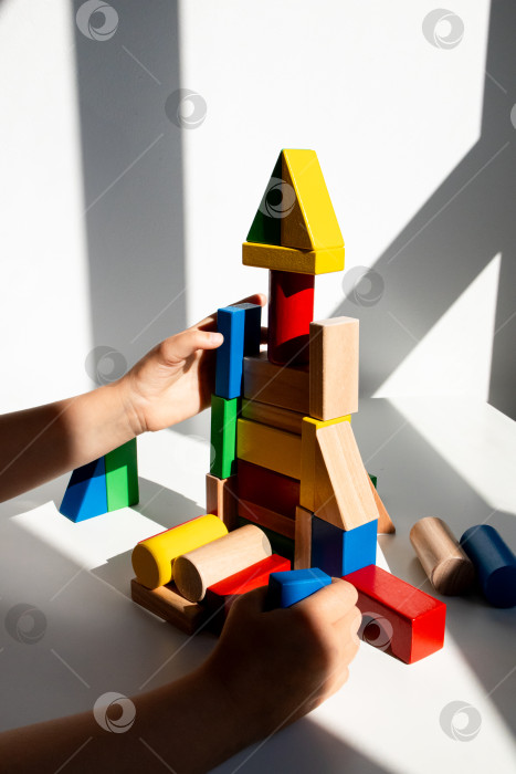 Скачать Ребенок играет с разноцветными деревянными кубиками при солнечном свете фотосток Ozero