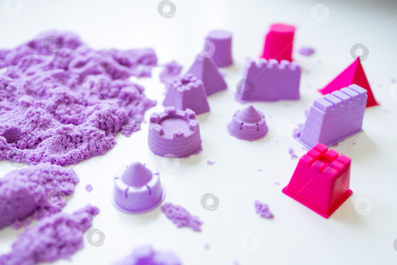 Скачать Фиолетовый кинетический песок с формочками для замков на белой поверхности фотосток Ozero