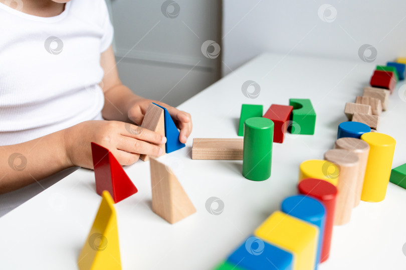 Скачать Ребенок играет с разноцветными деревянными геометрическими блоками на белой поверхности фотосток Ozero
