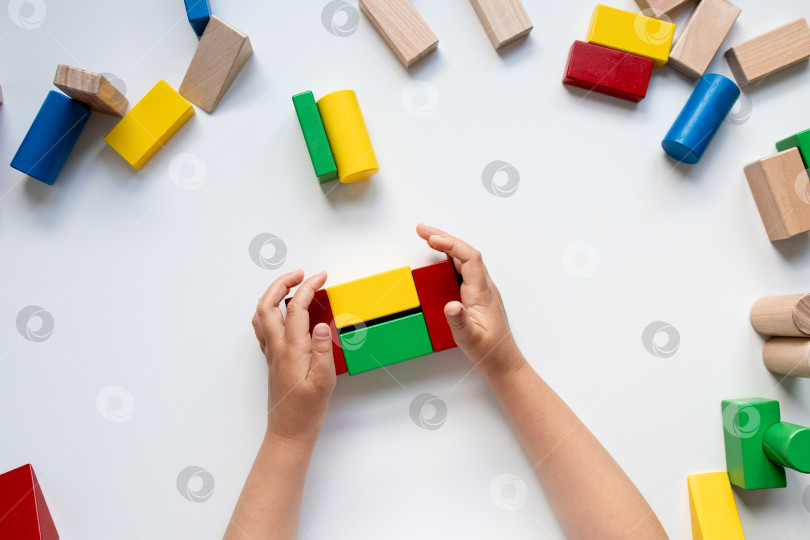 Скачать Ребенок своими руками строит дом из разноцветных деревянных кубиков на белой поверхности фотосток Ozero