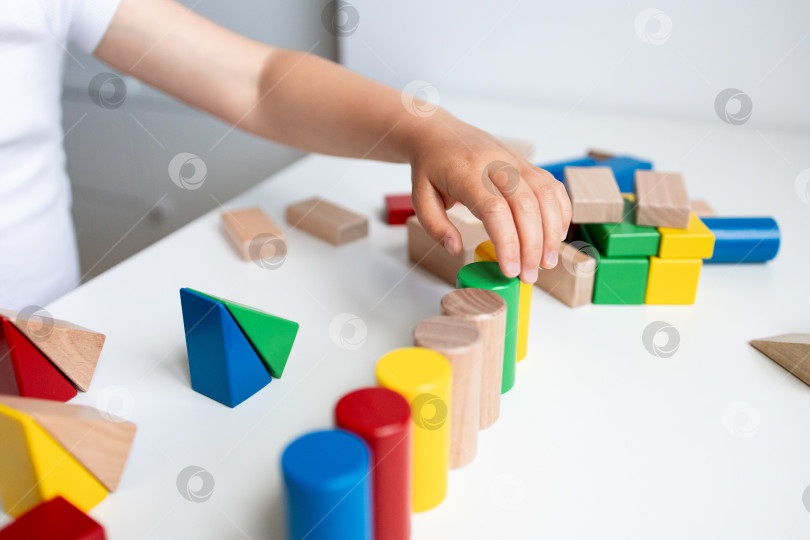 Скачать Ребенок играет с разноцветными геометрическими блоками на белом столе фотосток Ozero