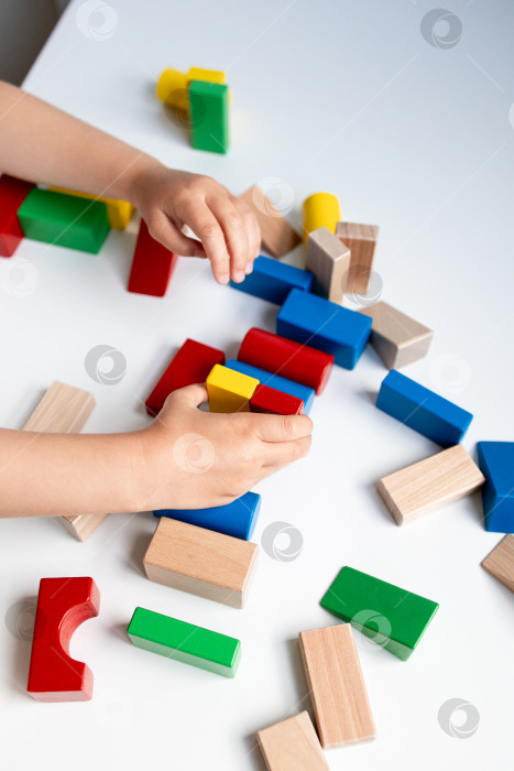 Скачать Ребенок играет с разноцветными деревянными строительными блоками на белой поверхности фотосток Ozero