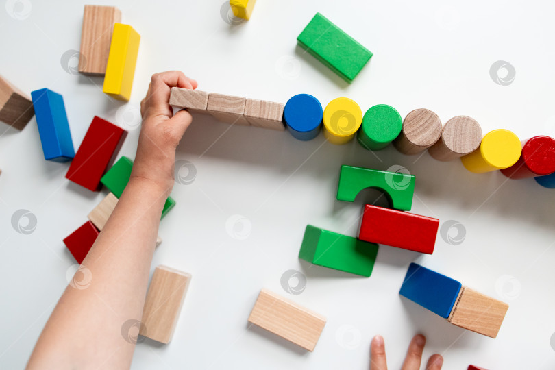 Скачать Ребенок играет с разноцветными деревянными кубиками на белой поверхности фотосток Ozero