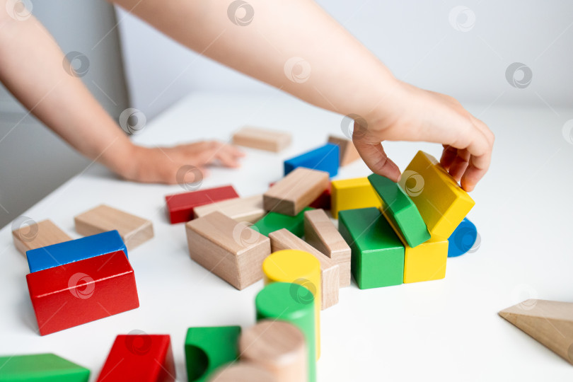 Скачать Ребенок играет с разноцветными деревянными кубиками на белом столе фотосток Ozero