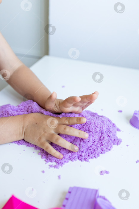 Скачать Ребенок играет с фиолетовым кинетическим песком на белом столе фотосток Ozero