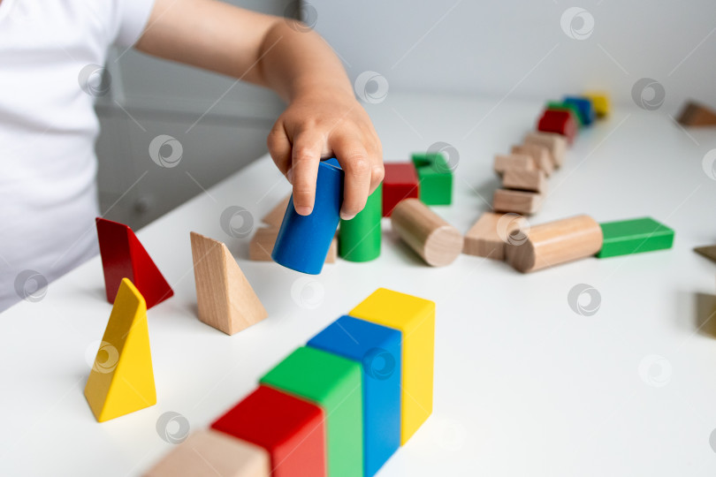 Скачать Ребенок играет с разноцветными геометрическими деревянными кубиками на белой поверхности фотосток Ozero