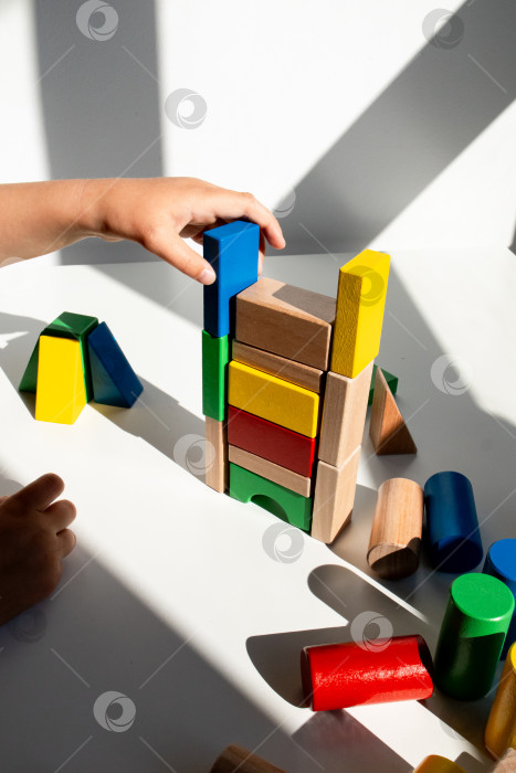 Скачать Ребенок строит башню из разноцветных деревянных блоков в залитой солнцем комнате фотосток Ozero