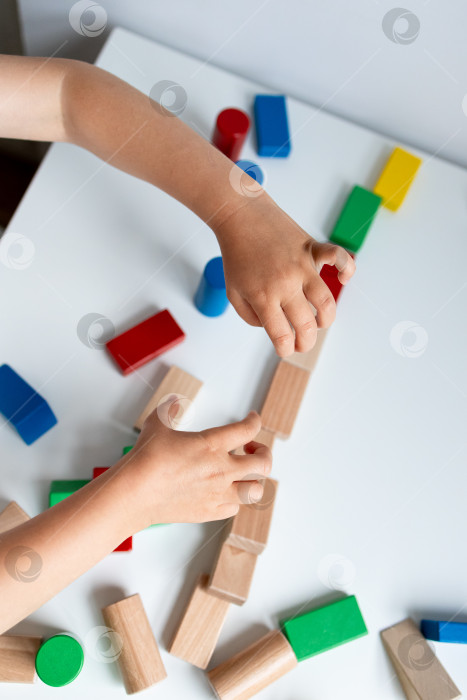 Скачать Ребенок играет с разноцветными деревянными кубиками на белом столе фотосток Ozero