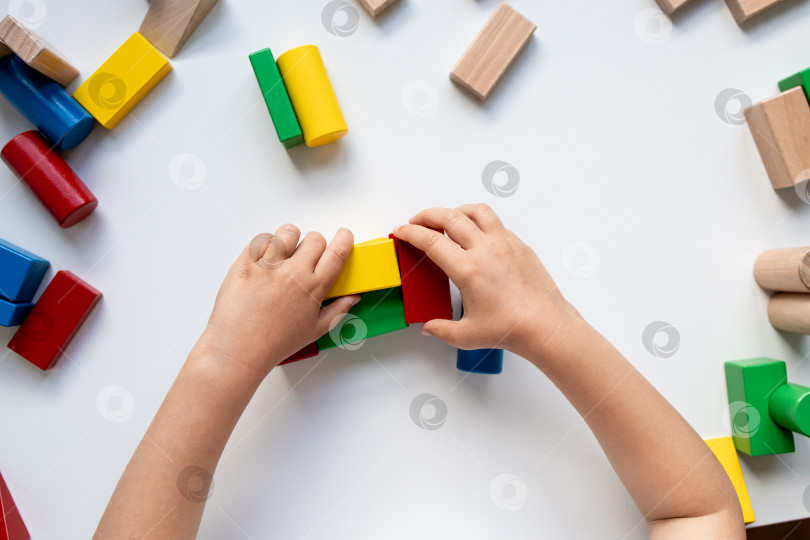 Скачать Ребенок своими руками строит здание из разноцветных деревянных блоков на белой поверхности фотосток Ozero