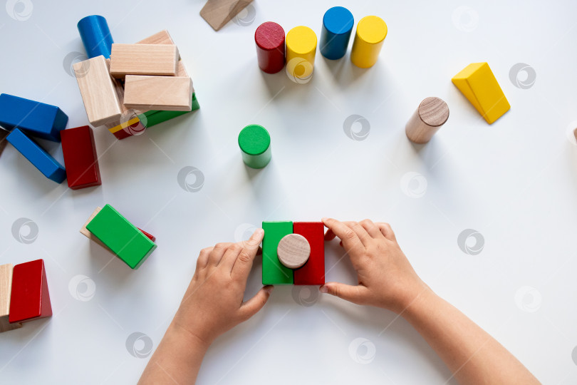 Скачать Детские ручки играют с разноцветными деревянными кубиками на белой поверхности фотосток Ozero