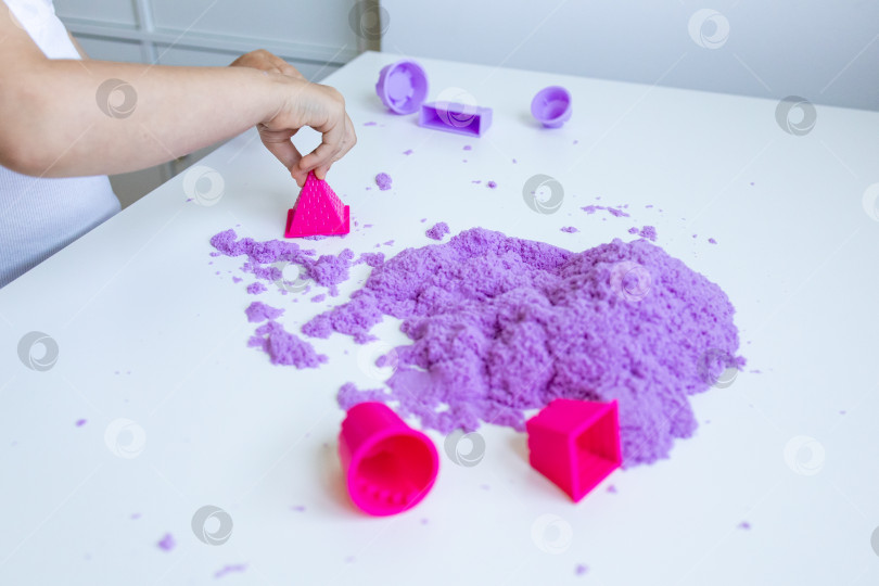 Скачать Детская рука играет с фиолетовым песком и формочками на белом столе фотосток Ozero