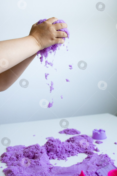 Скачать Ребенок играет с фиолетовым кинетическим песком на белом столе фотосток Ozero