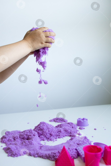Скачать Ребенок играет с фиолетовым кинетическим песком на белой поверхности фотосток Ozero