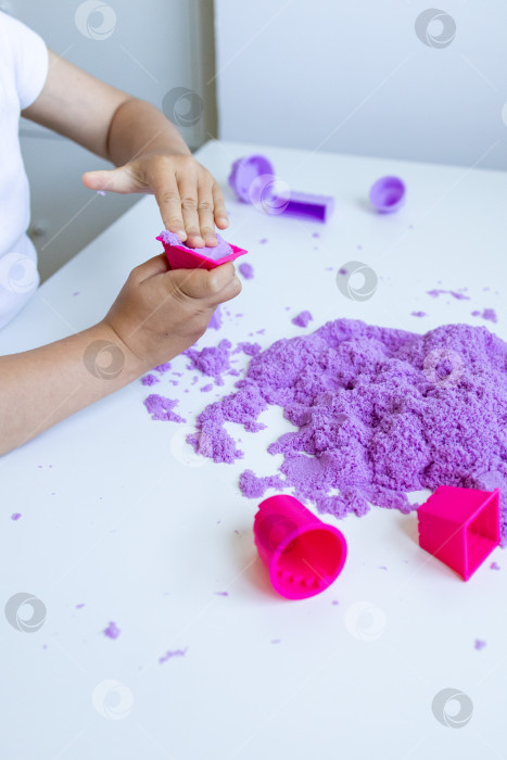 Скачать Ребенок играет с фиолетовым кинетическим песком на белом столе фотосток Ozero