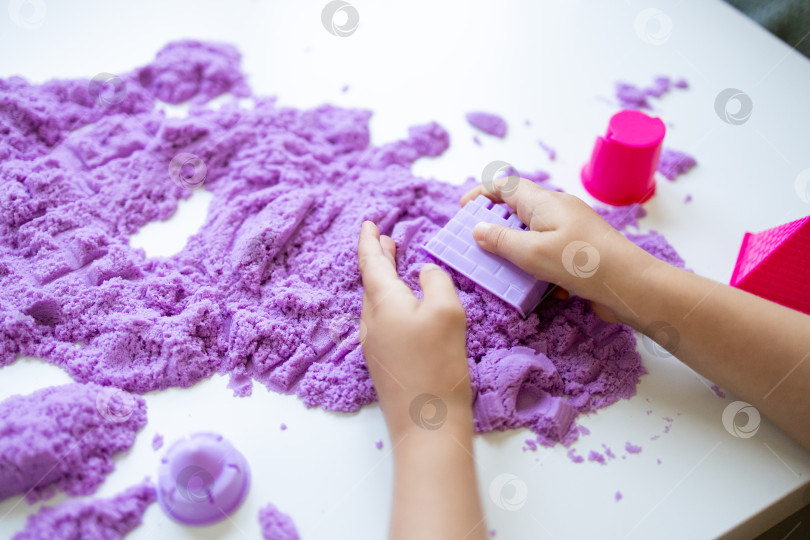 Скачать Ребенок играет с фиолетовым кинетическим песком и формочками на белом столе фотосток Ozero