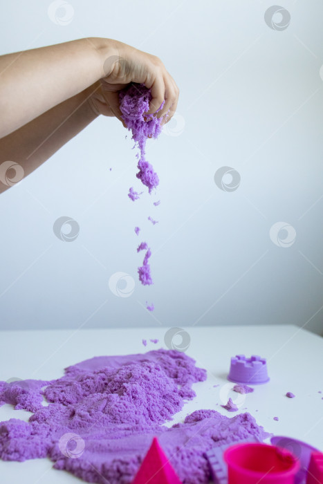 Скачать Ребенок играет с фиолетовым кинетическим песком на белой поверхности фотосток Ozero