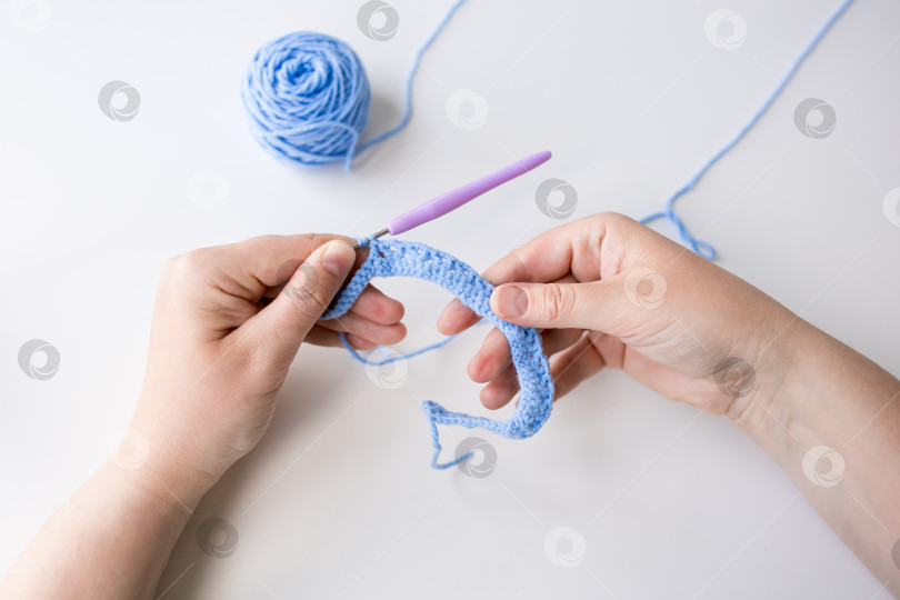 Скачать Крупным планом женские руки, вяжущие крючком из голубой пряжи на белом фоне фотосток Ozero