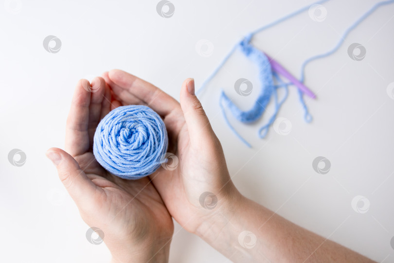Скачать Женщина держит в руках клубок голубой пряжи с крючками для вязания крючком на белом фоне фотосток Ozero