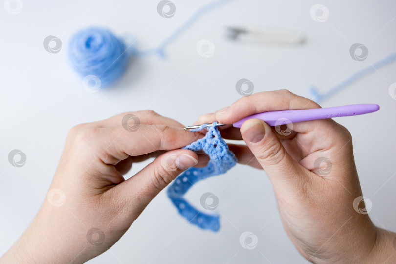 Скачать Крупный план рук, связанных крючком фиолетовым крючком и синей пряжей фотосток Ozero