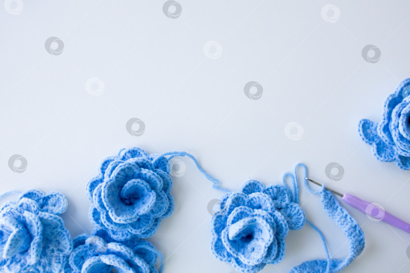 Скачать Синие вязаные цветы и крючок на белом фоне. Выставка замысловатых поделок ручной работы фотосток Ozero