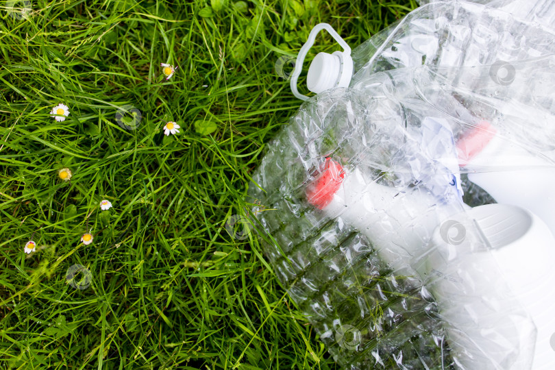 Скачать Раздавленная пластиковая бутылка на траве с маргаритками, подчеркивающими воздействие на окружающую среду фотосток Ozero