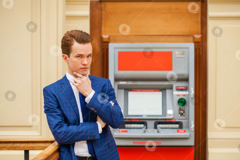 Скачать Бизнесмен в синем костюме стоит на фоне банкомата в торговом центре фотосток Ozero