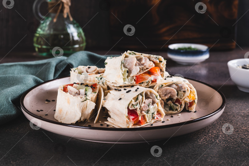 Скачать Куриное мясо, перец и огурец в соусе, завернутые в рулетики из тортильи, на тарелке на столе фотосток Ozero