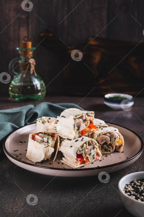 Скачать Куриное мясо, перец и огурец в соусе, завернутые в рулетики из тортильи, на тарелке в вертикальном положении фотосток Ozero