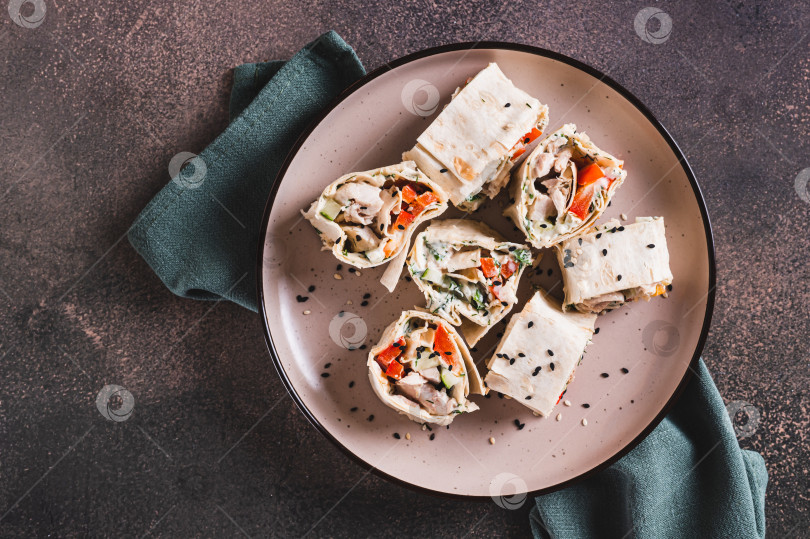 Скачать Крупным планом куриное мясо, перец и огурец в соусе, завернутые в рулетики из тортильи, на тарелке, вид сверху фотосток Ozero
