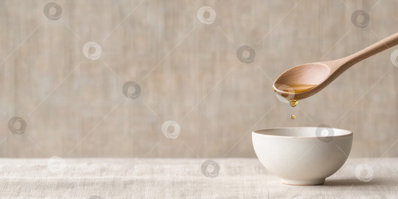 Скачать Крупный план золотистой капли рапсового масла, падающей с деревянной ложки в миску на льняную поверхность. фотосток Ozero