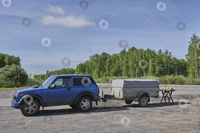 Скачать Рядом с автомобилем с грузовым прицепом стоит небольшой столик с несколькими баночками меда. Продажа продуктов пчеловодства фотосток Ozero