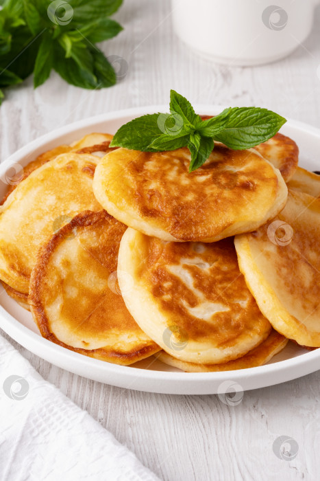 Скачать Вкусные золотистые блинчики подаются со свежими листьями мяты на белой тарелке в уютной кухне фотосток Ozero