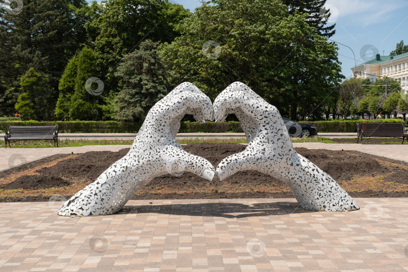 Скачать Скульптура в форме сердца, сделанная из рук, в общественном парке с деревьями и скамейками в дневное время - Ставрополь, Россия, 1 июня 2025 года фотосток Ozero